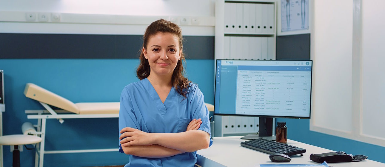 Nurse with arms crossed standing in front of computer